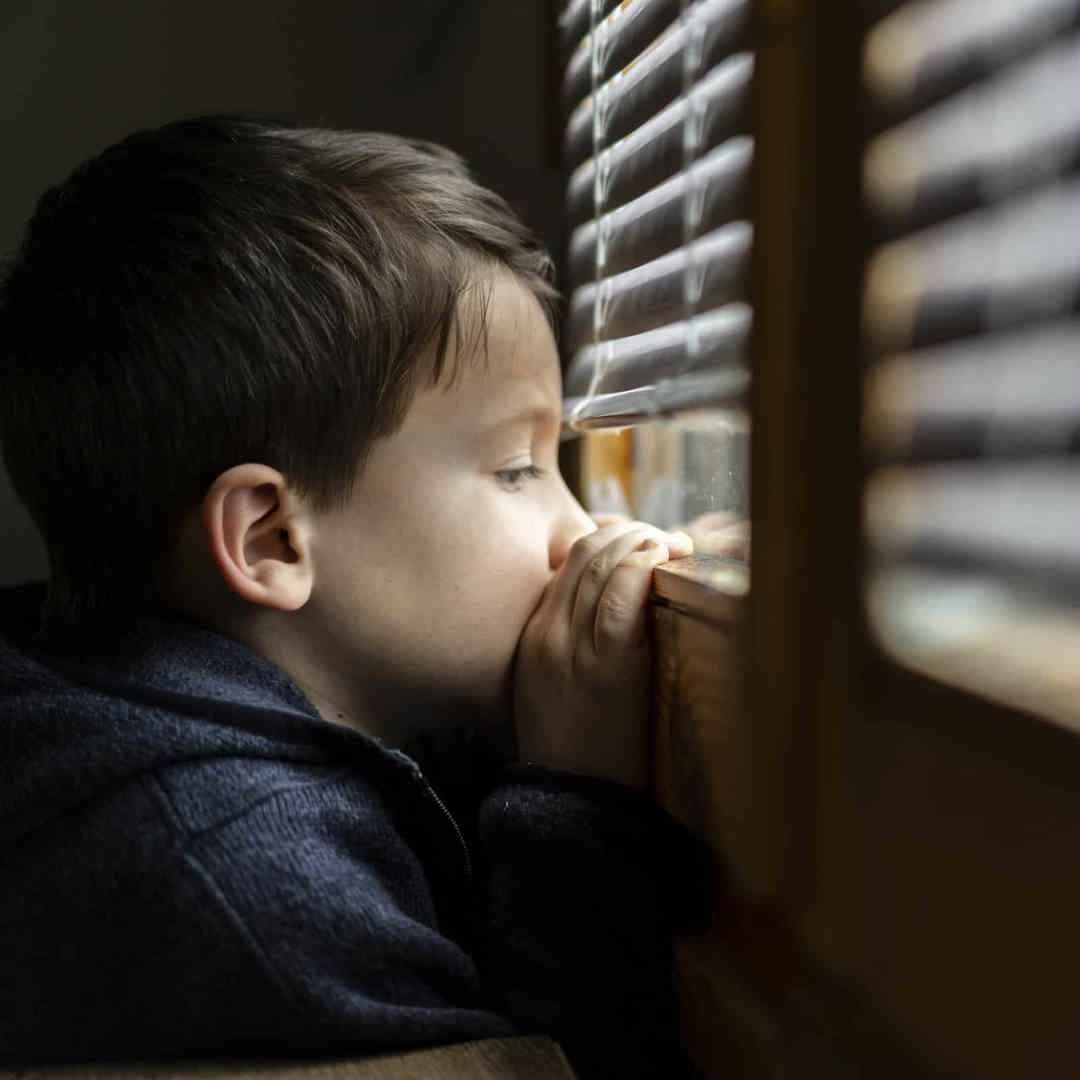 Rouwend kind kijkt door de kieren van een rolluik: zo help je kinderen bij verlies