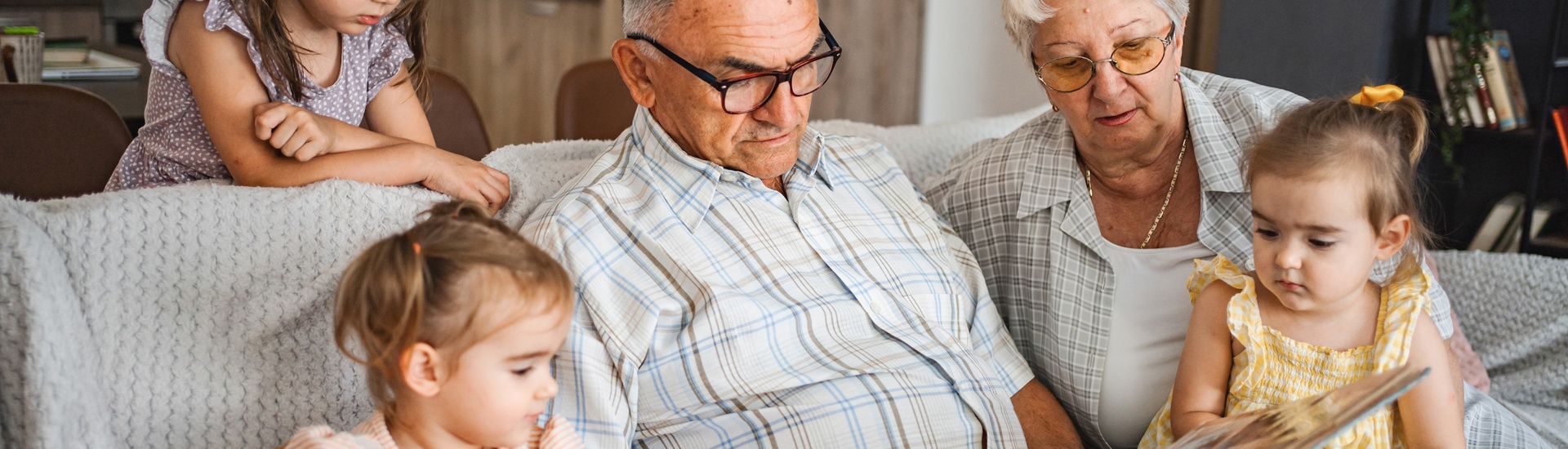 Oma en opa in hun rol als grootouders tijdens een voorleesmoment met hun kleinkinderen op de zetel